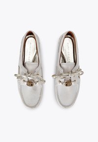 Scarpe slip-on argento con finitura testurizzata, caratterizzate da un fiocco decorativo e hardware in tonalità oro. Punta arrotondata e dettagli di cucitura discreti.