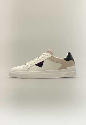 Baskets basses en cuir blanc avec talon en daim beige, languette de talon noire et patch logo triangulaire bleu marine avec texte rouge "Replay" sur le côté.