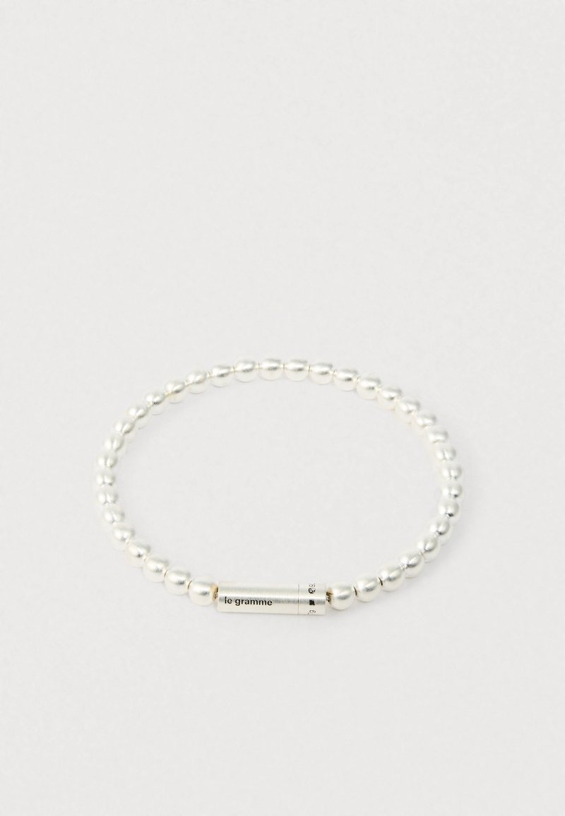 Hõbedane helkearmastusega käevõru, millel on silindriline klipp, millele on graveeritud "le gramme," esitatud lihtsal valgel taustal.