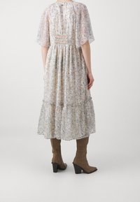 Floral-patterned maxi dress with short, sheer sleeves, smocked back, and tiered skirt. Worn with knee-high brown suede boots.