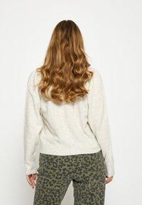 Svetlosivý pletený sveter s rebrovanými manžetami a lemom, v kombinácii so svetlozelenými nohavicami so vzorom leopardej potlače, ktoré majú pohodlný strih a mäkkú textúru.