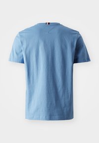 Jasnoniebieska bawełniana koszulka z krótkim rękawem, dekoltem w serek i małym paskiem z tyłu szyi. Gładka tekstura, casualowy design.