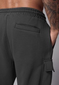 Mörkgrå sweatpants med elastisk midja, sidofickor och en ficka på vänster lår. Slät tygstruktur.