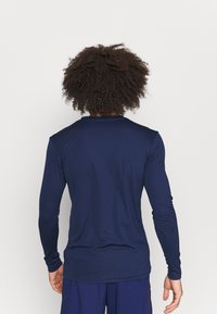 Laadukas tummansininen pitkähihainen urheilupaita, joka on valmistettu joustavasta kankaasta. Paidassa on pyöreä pääntie ja tiukka siluetti. Sileä pinta ja minimalistinen muotoilu.