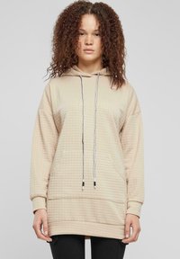 Sweat-shirt beige à capuche avec un motif texturé, une poche kangourou et des cordons réglables. Manches longues avec une coupe décontractée.