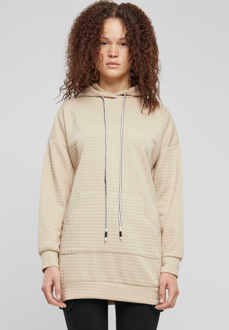 Sweat-shirt beige à capuche avec un motif texturé, une poche kangourou et des cordons réglables. Manches longues avec une coupe décontractée.