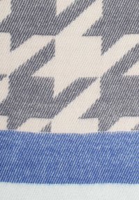 Textil mit beigem Hintergrund und grauen Zickzackmustern sowie einem blauen horizontalen Streifen am unteren Ende. Glatte, gewebte Textur.