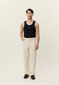 Crni top bez rukava s bijelim logotipom, uparen s kremasti širokim hlačama i smeđim cipelama. Glatka tekstura i jednostavan dizajn, bez uzoraka.