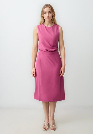 Fuchsia mouwloze jurk met een gedrapeerde halslijn, gladde textuur en midi-lengte, gecombineerd met lichte sandalen met bandjes.