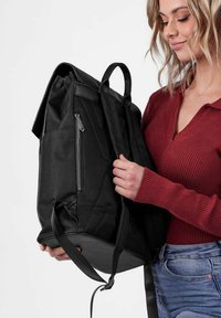 Černý batoh s texturovaným povrchem, obsahující boční síťovanou kapsu, přední zipy a dva nastavitelné popruhy. Ozdobený robustním podstavcem.
