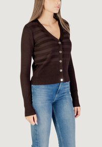 Cárdigan marrón a rayas con un profundo escote en V, puños acanalados y seis botones frontales con acentos metálicos, combinado con jeans azules.