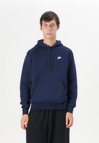 Sweatshirt com capuz azul marinho feito de um material suave, apresentando um bolso frontal e um logótipo Nike branco no peito. Mangas longas com punhos canelados.