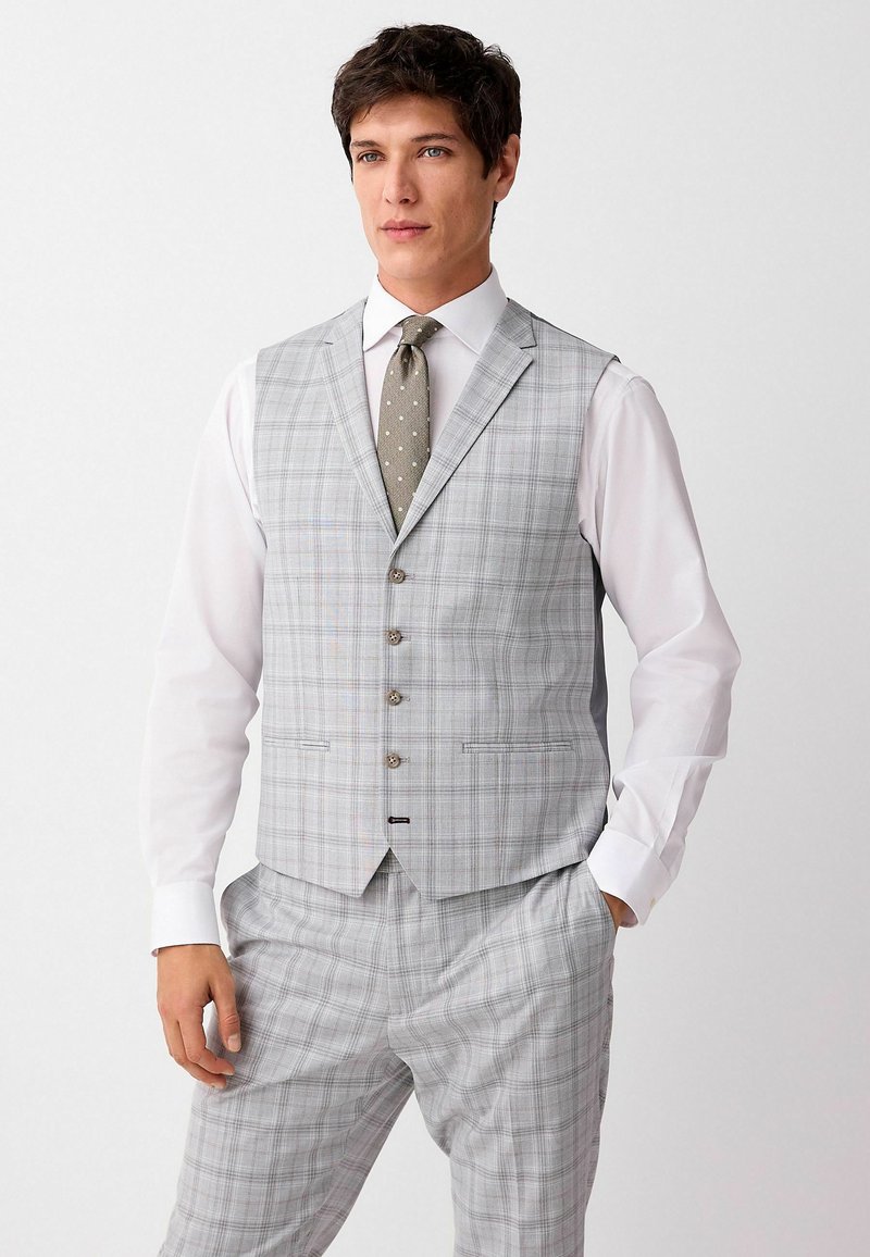 Light gray plaid vest with a fitted design, five buttons, and pointed lapels, paired with a white long-sleeve shirt and textured green tie.