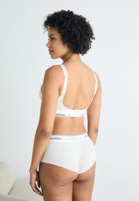 Ελαφρύ μπεζ σουτιέν Calvin Klein με ρυθμιζόμενες τιράντες και κλείσιμο με γάντζο, σε συνδυασμό με λευκά ψηλόμεσα σλιπ με ελαστική ζώνη που φέρει το λογότυπο.