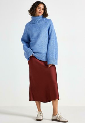 Lyseblå chunky striktrøje med høj hals, parret med en bordeaux satin-nederdel og beige sneakers, som fremhæver kontrasterende teksturer.