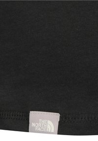 Černé bavlněné tričko s prošívaným lemem, měkkou texturou a viditelnou etiketou "The North Face" v světle šedé na spodním okraji.