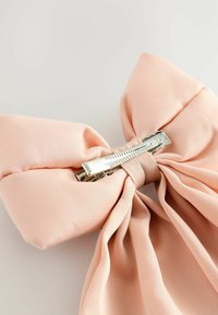 Un nœud en satin rose clair avec une pince en métal au centre, présentant une texture lisse et un tissu soigneusement drapé.