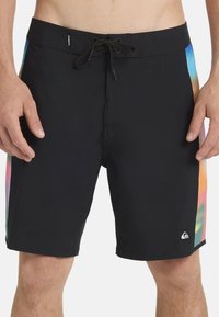 Costum de baie negru, cu un panou lateral în gradient curcubeu. Are un material durabil, talie cu șnur și un logo mic pe piciorul inferior.