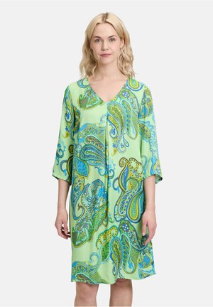 Hellgrünes Kleid mit V-Ausschnitt und dreiviertel Ärmeln, mit einem bunten Paisley-Muster in Blau- und Gelbtönen. Glatte Stoffstruktur.