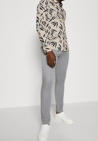Beige shirt with black leaf print, long sleeves, button-up front, paired with light gray slim-fit pants and white sneakers.