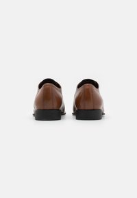 Scarpe in pelle marrone con una finitura liscia, punta tondeggiante e suola in gomma nera. Design minimalista con linee pulite e senza decorazioni visibili.