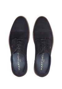 Un paio di scarpe eleganti in suede blu navy con suole marroni, viste dall'alto, che mostrano le solette "Martinelli 1973" in lettere dorate.