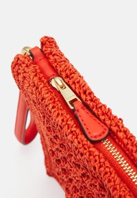 Czerwona, pleciona torebka z złotym zamkiem i skórzanym uchwytem do zamka, pokazana z bliska na białym tle.
