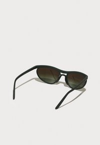 Ochelari de soare din plastic negru, cu lentile ovale, cu un gradient întunecat. Brațe subțiri cu o ușoară curbă, având un branding discret pe o parte.