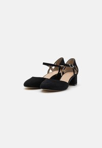 Chaussures Mary Jane en daim noir avec un bout rond, une bride à la cheville et un talon carré. Présente des sangles croisées pour un détail supplémentaire.
