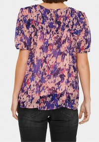 Blus med blommönster i nyanser av rosa, lila och blått, med korta puffärmar och en knappdetalj på ryggen. Lättviktigt tyg.