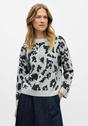 Pull gris avec motif léopard noir, col rond et manches longues. Texture douce et coupe légèrement ample. Porté avec un denim foncé.