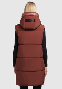 Vest pufos maro cu guler înalt, având o capotă lucioasă și cusături orizontale. Materialul pare neted, cu un logo pe spate.