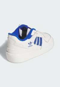 White sneaker with blue accents, leather upper, textured stitching, padded collar, and rubber sole. Features three blue stripes on the side.