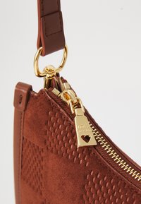 Braune Wildleder-Handtasche mit strukturiertem Muster, goldener Reißverschluss und herzförmigem Anhänger mit der Gravur "LOVE MOSCHINO" sowie passendem Riemenanschluss.