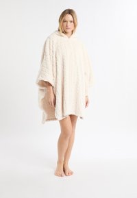 Poncho beige chiaro con cappuccio, realizzato in materiale morbido e strutturato con motivo a diamante e maniche corte, che arriva sopra il ginocchio.