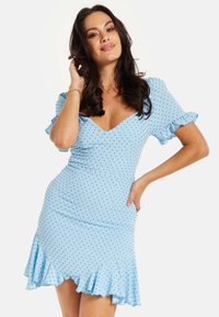 Light blue polka dot dress with short ruffled sleeves, a deep V-neck, fitted waist, and a flared hem. Made from a stretch fabric.