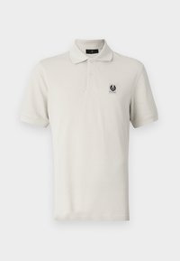 Polo beige en coton, avec un col classique, des manches courtes et un petit patch logo noir sur la poitrine gauche.