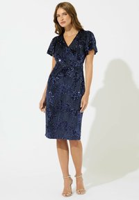Marineblaues, mit Pailletten besetztes Kleid mit figurnaher Silhouette, kurzen, schwingenden Ärmeln und tiefem V-Ausschnitt, das ein strukturiertes Muster aufweist.