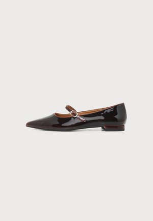 Chaussure plate Mary Jane en cuir verni noir avec bout pointu et petite bride à boucle sur le côté, sur fond blanc.