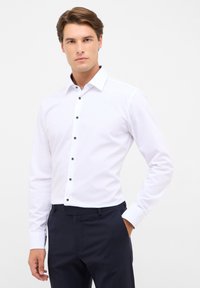 Witte overhemd met lange mouwen en een spread collar, voorzien van zwarte knopen langs de sluiting en een zachte textuur, gecombineerd met donkere broeken.