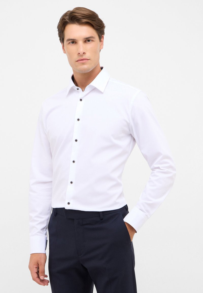 Witte overhemd met lange mouwen en een spread collar, voorzien van zwarte knopen langs de sluiting en een zachte textuur, gecombineerd met donkere broeken.