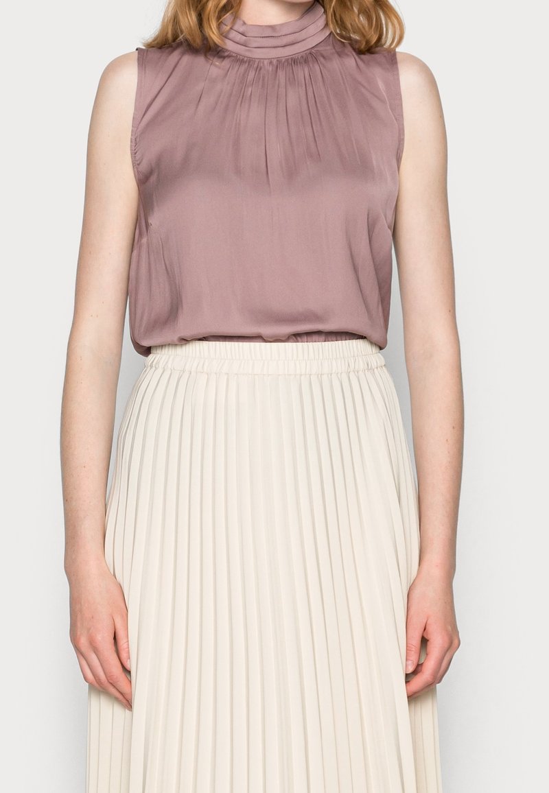 Halenka bez rukávů v popelavě růžové barvě s plisovanými detaily na výstřihu, v kombinaci se krémovou plisovanou sukní s elastickým pasem.