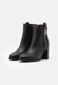 Bottines en cuir noir à bout pointu, avec une fermeture éclair dorée sur le côté et un panneau texturé noir. Présente un talon épais pour plus de stabilité.