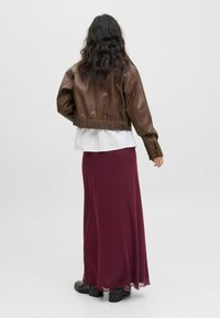 Chaqueta de cuero marrón cortada sobre una blusa blanca en capas, combinada con una falda larga burdeos con un dobladillo festoneado, y botas negras.