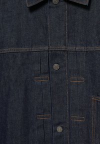 Tamnosivi traper košulja s ovratnikom, koja ima kontrastno narančasto šivanje, šest gumba i dvije horizontalne džepove. Tekstuirana tkanina.