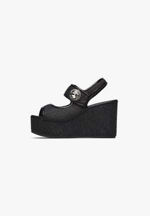 Sandalo con zeppa nero con cinturini texturizzati, punta aperta, cinturino sul tallone e una grande gemma decorativa trasparente sulla fascia anteriore.