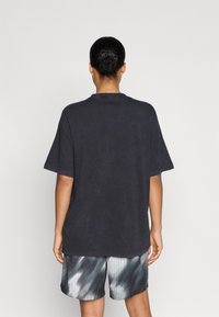 Tricou negru din bumbac cu croială lejeră, mâneci scurte și decolteu rotund. Asortat cu pantaloni scurți din plasă gri, cu un model subtil.