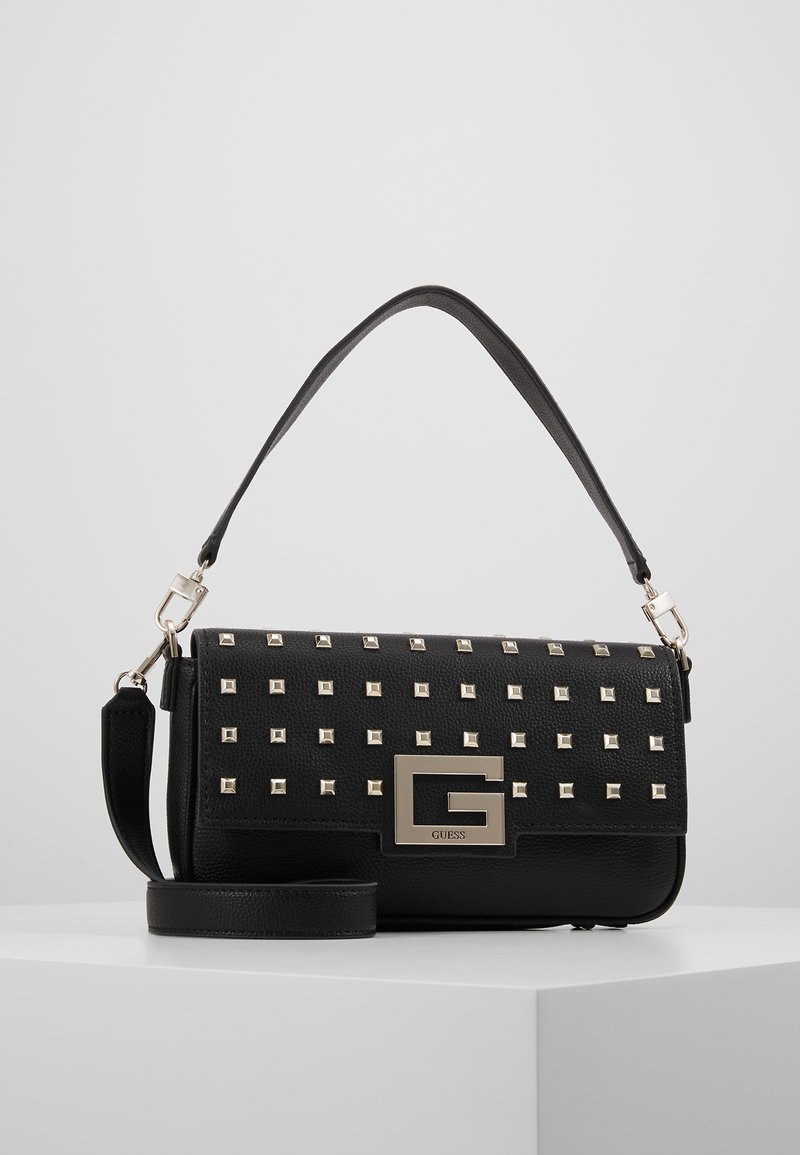 Sort læderhåndtaske med metalliske nitter, en aftagelig skulderrem og en fremtrædende sølvlogo-plade på fronten.