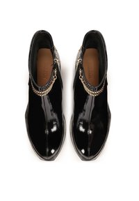 Bottines en cuir verni noir avec un bout pointu, fermeture éclair sur le côté, et un accent en chaîne dorée autour de la cheville. Texture lisse et brillante.