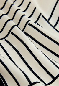 Tissu crème avec des rayures noires verticales et horizontales espacées régulièrement formant un motif en grille, présenté en plis doux.